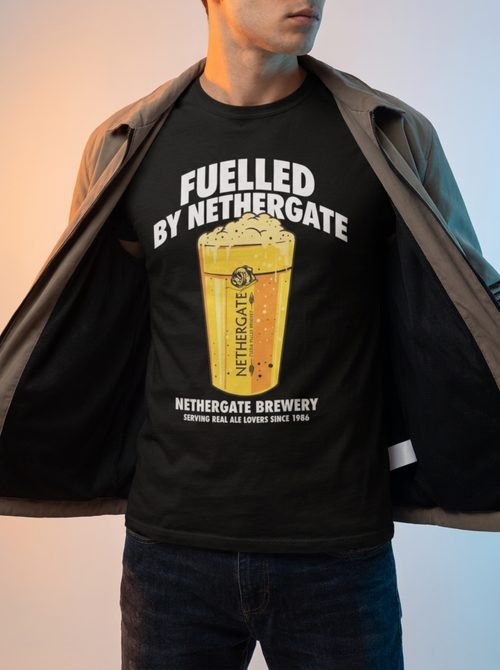 Model holding open a jacket to reveal a Fuelled by Nethergate Brewery printed black t-shirt under coloured studio gels
