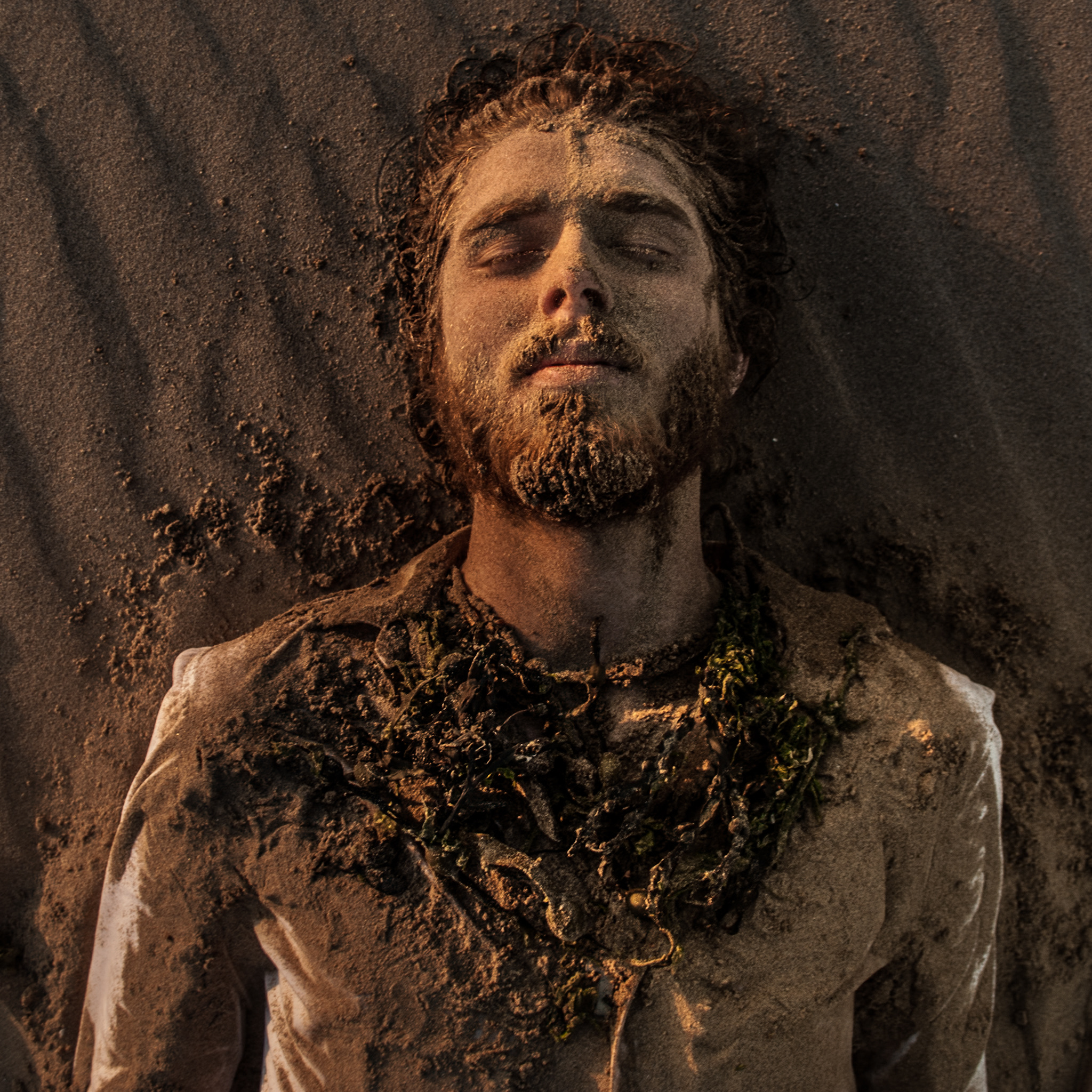 Anchor photograph — figure half-buried in sand with a seaweed collar